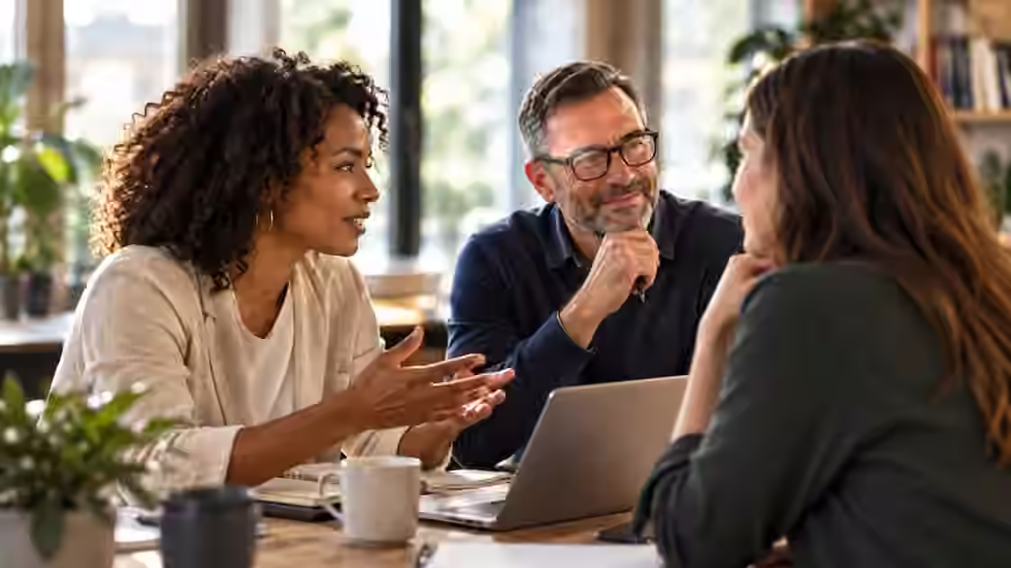 Three people discussing a piece of work together around a laptop in a bright office.